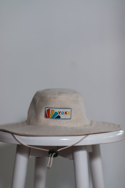Wide brim drawstring hat. Placed on stool to display. Featuring brand label at the front. 